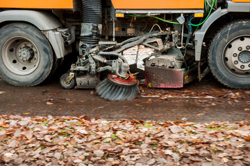 Orange street sweeper machine cleaning the street from fall foliage
