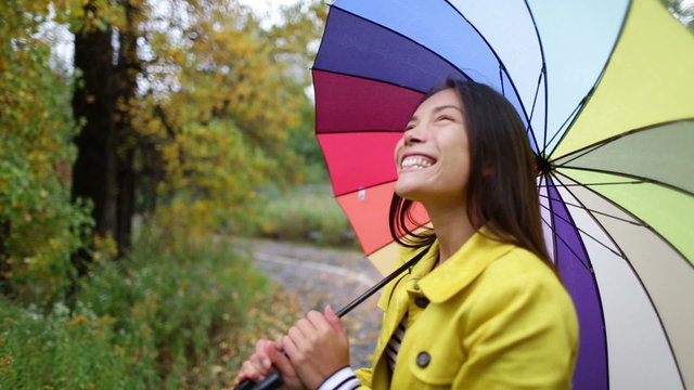 Fall / Autumn concept - woman excited under rain with umbrella. Beautiful young female wearing raincoat surprised and excited in the rain. Mixed race Asian Caucasian girl in her 20s walking in forest.