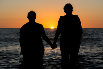 Sunset backlighting silhouette of two women in the beach holding hands