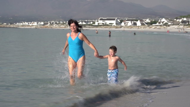 Mother and young boy running towards camera through shallow water on beach, Cape Town,South Africa