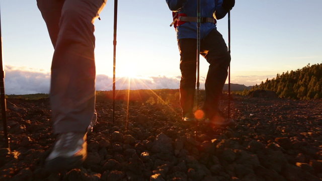 Hiking shoes on hikers walking at sunset. Man and woman hiker hike boots in closeup while trekking with hiking poles.
