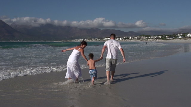 Slow motion of couple swinging child in the shallow waters of the beach, Cape Town,South Africa