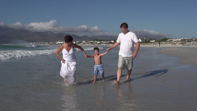Slow motion of couple swinging child in the shallow waters of the beach, Cape Town,South Africa