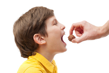 A kid tries to bite chocolate ball in man hand, isolated on white background