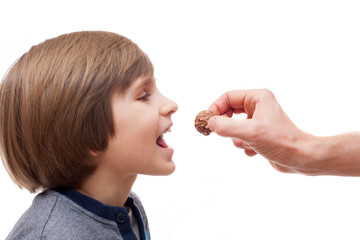 A small boy bites chocolate ball from man hand
