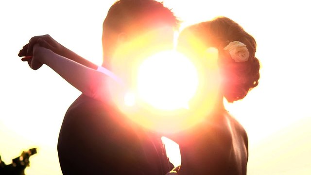 Pair of backlit newlyweds face to face with the sun going explodes between them.
