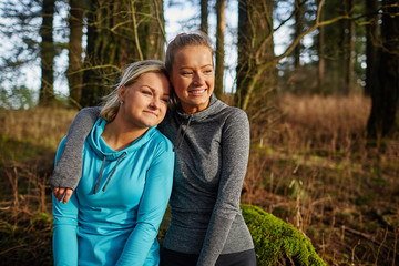 Fototapeta premium two beautiful young girls sitting on log arms around watching su