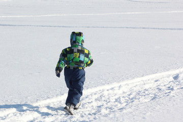 Fototapeta na wymiar The child in a color jacket running on snow in the winter