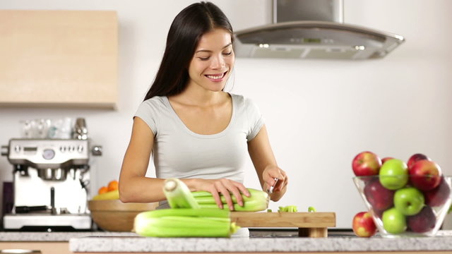 Woman cutting vegetables making food in kitchen. Happy smiling asian girl cutting celery with knife on cutting board at home.