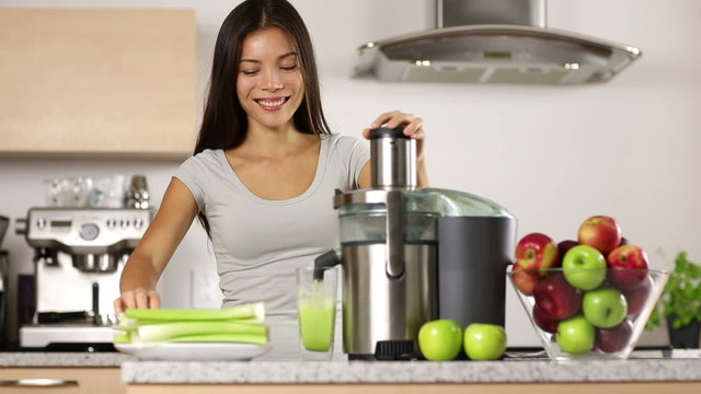 Vegetable juice raw food - healthy eating woman with juicer juicing celery, green vegetables and apple fruits and drinking glass of green juice. happy mixed Asian woman with juice maker in kitchen.