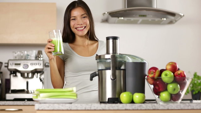 Woman making green vegetable juice and drinking it fresh at home in kitchen giving thumbs up. Juicing and healthy eating happy woman making green vegetable and fruit juice.
