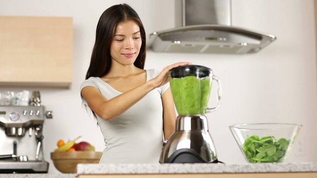 Green smoothie woman making vegetable smoothies with blender. Healthy eating lifestyle concept portrait of beautiful young woman preparing drink blending spinach, carrots, celery at home in kitchen.