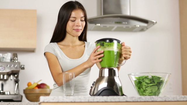 Woman making, pouring, drinking green vegetable smoothie with blender. Healthy eating lifestyle with young woman preparing blending smooithies drink with spinach, carrots, celery at home in kitchen.