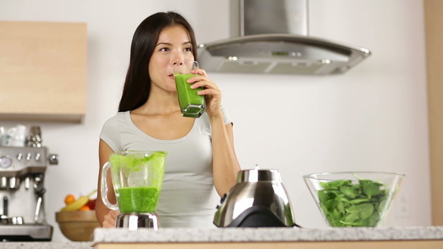 Green smoothie woman drinking vegetable smoothies giving thumbs up looking at camera. Healthy eating lifestyle young woman having drink with spinach, carrots, celery with blender at home in kitchen.