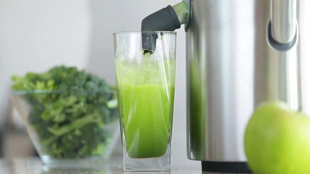 Juicing machine making broccoli vegetable juice. Close up of juicer maker and green juice in fast forward motion.