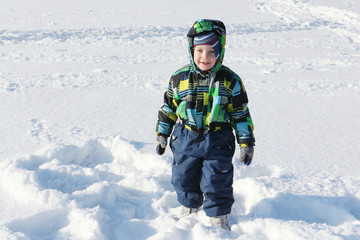 Fototapeta na wymiar Portrait of the little boy in a color jacket against snow in the winter