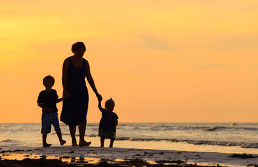 Fototapeta premium mother and two kids walking on beach at sunset