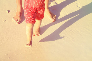 Mother and baby feet walking on sand beach