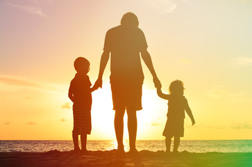 father and two kids walking on beach at sunset