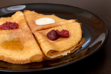 Pancakes with strawberry jam, raspberry jam , sour cream and honey on a black plate