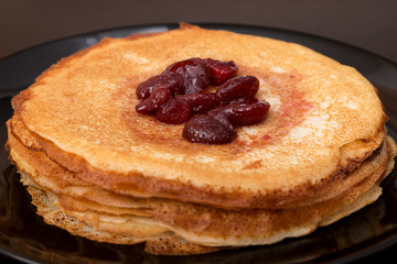 Pancakes with strawberry jam on a black plate