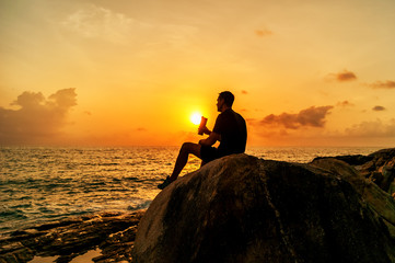 Silhouette of man sitting on the rocks by the sea at dawn
