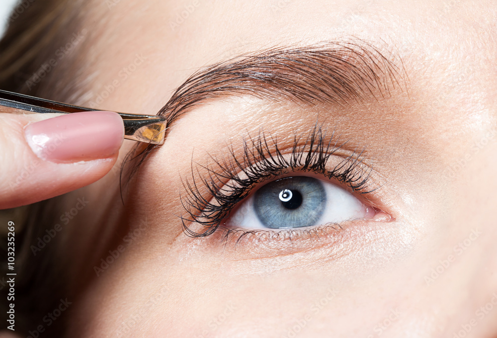 Wall mural closeup of a woman pulls out her eyebrows with tweezers