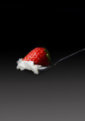 Whipped cream and a strawberry in a silver spoon on black backgr