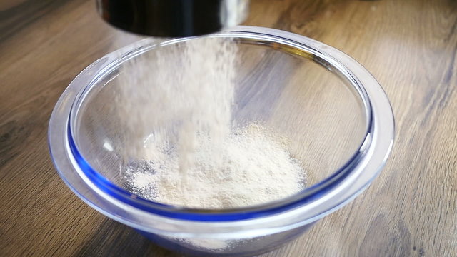 Close up of a fine curtain of refined white cake flour falling through a metal sieve