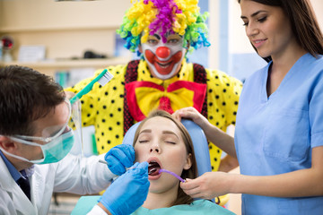 Girl repair tooth in dental clinic with clown in background