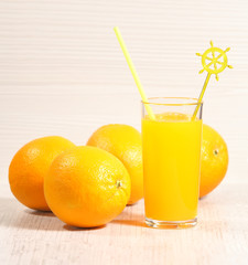 Fresh orange lemonade in a glass next to the whole fruit and orange slices on a light gray background. Selective focus