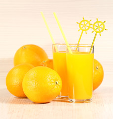 Fresh orange lemonade in a glass next to the whole fruit and orange slices on a light gray background. Selective focus