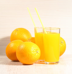 Fresh orange lemonade in a glass next to the whole fruit and orange slices on a light gray background. Selective focus
