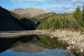 Mountain river and reflection in the water peaks. River Omulevka. Magadan Region. Russia.