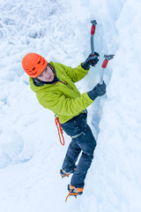 Alpinist man with  ice tools axe in orange helmet climbing a lar