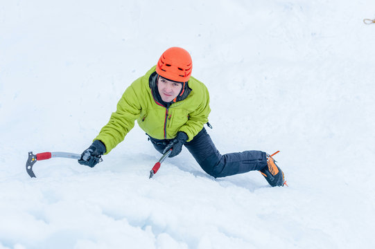 Ice climber man with  ice tools axe in orange helmet climbing a