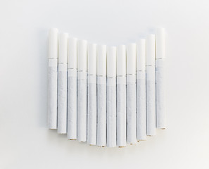 Cigarette with a white filter laid out in a row on a white backg