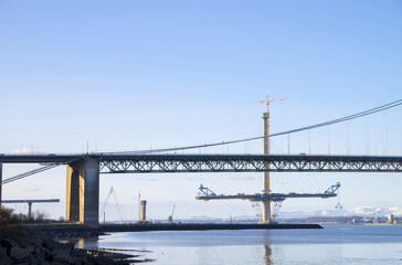 The South Queensferry end of the Forth Road Bridge, with a partially-completed tower and deck of the new Queensferry Crossing in the background