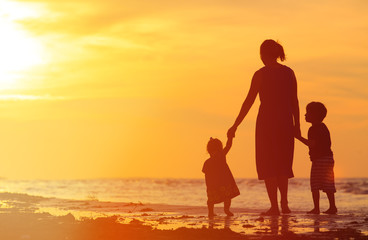 Fototapeta premium mother and two kids walking on beach at sunset