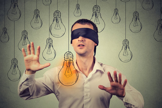 Blindfolded young man walking through light bulbs searching for bright idea