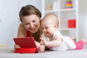 Family - mother and baby with tablet on floor at home. Woman and child girl relaxing at tablet...