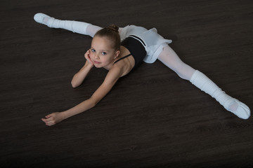 A little adorable young ballerina doing stretching exercises on