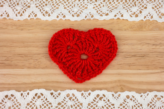 Knitted heart on wooden background with lace.
