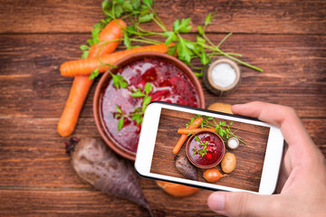 Hands taking photo red beetroot soup with smartphone. Concept of cooking .