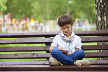 A little boy sits on a bench and calling by mobile phone