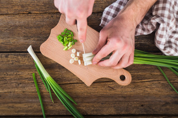 man chopped green onion on the board. Wooden table