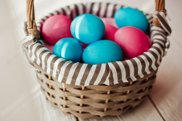 Fototapeta na wymiar Multicolored Easter eggs in wicker basket on white wooden background