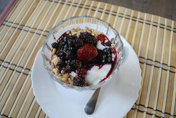 Berries (strawberries, blueberries, blackberries) dessert with yogurt and rice flakes in glass cup. Finished dish.