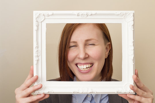 Happy smiling beautiful woman looking through a white picture frame.