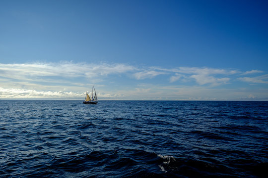 Segelschiff, Zweimaster, leuchtend weiß, auf weiter blauer, klarer Wasserfläche